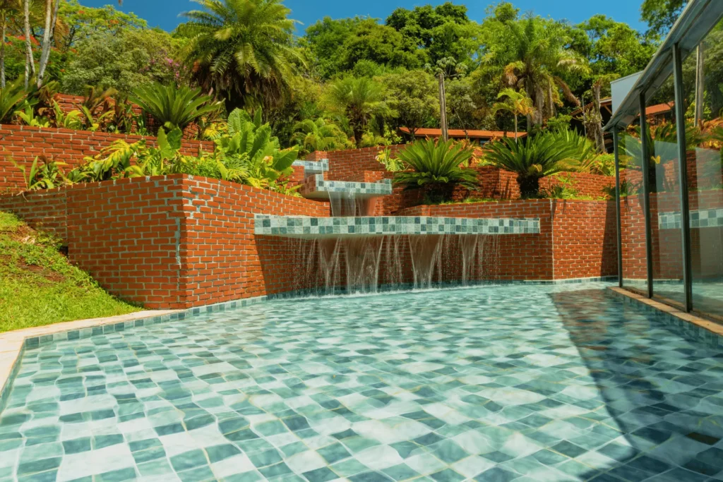 Fonte decorativa com quedas d'água em estrutura de tijolos e azulejos, cercada por jardim tropical no Hotel Colonial Iguaçu.